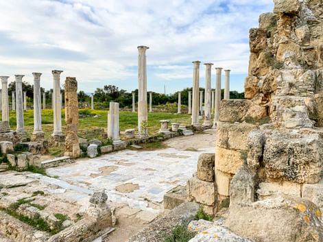 Antike archäologische Stätte von Salamis auf Zypern mit weißen Marmorsäulen, Steinruinen und gepflasterten Böden unter bewölktem Himmel.