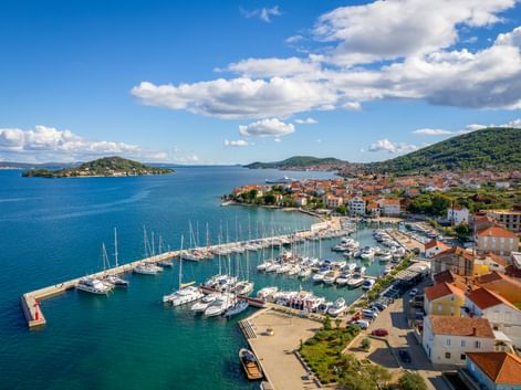 Aerial view of Preko marina on Ugljan Island with sailboats, red-roofed houses, and green hills along the Adriatic coast in North Dalmatia.