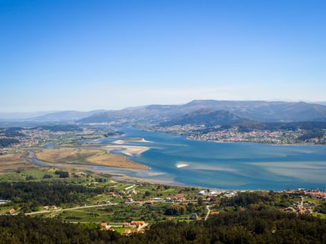 Luftaufnahme der Minho-Flussmündung mit blauem Wasser, Sandbänken, grünen Feldern und Küstendörfern. Berge erheben sich im Hintergrund.