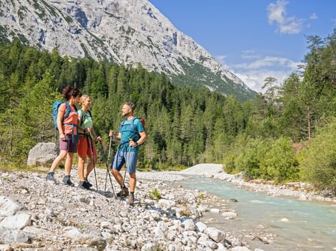 Drei Wanderer mit Rucksäcken und Wanderstöcken stehen an der türkisfarbenen Leutascher Ache in der Zugspitzregion vor Kalksteinfelsen.