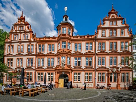 Baroque facade of the Gutenberg Museum in Mainz with ornate orange-white architecture, stepped gables, and central tower under blue sky.