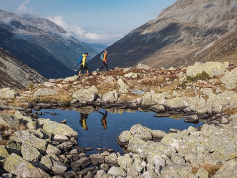 Spiegelung zweier Wanderer im Bergsee mit Panorama