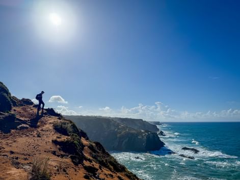 Wanderer auf Küstenklippenpfad mit Blick auf den Atlantik bei Almograve. Dramatische Klippen erstrecken sich entlang türkisfarbenem Wasser.