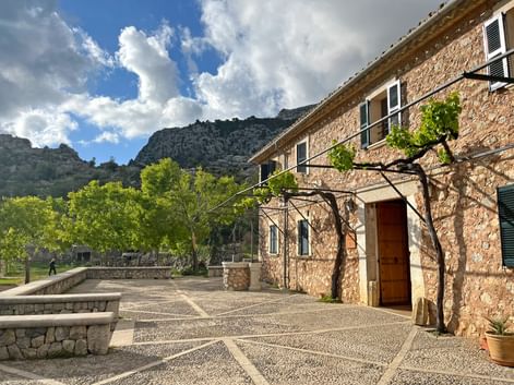 Stone building Refugi Tossals Verds with patterned courtyard, vine-covered entrance, and mountain backdrop on Mallorca's GR221 trail.