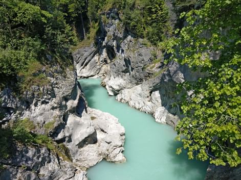 Luftaufnahme des türkisfarbenen Lech, der durch eine enge felsige Schlucht fließt, umgeben von dichtem grünen Wald und großen Kalksteinblöcken.