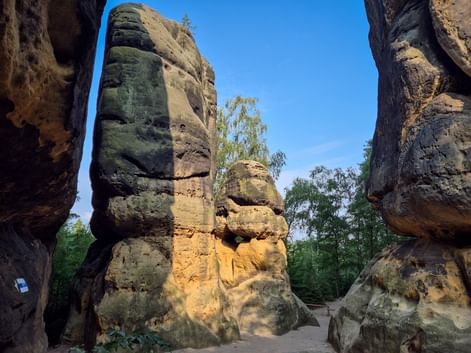Blick durch enge Passage zwischen hohen Sandsteinfelsen am Schrammtor auf dem Malerweg, mit moosbewachsenen Oberflächen und blauem Himmel.
