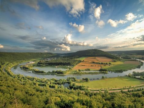 Luftaufnahme des Altmühltals mit einem sich windenden Fluss, der eine Schleife um grüne Felder und Wälder bildet, unter blauem Himmel mit weißen Wolken.