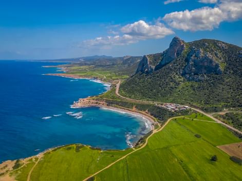 Luftaufnahme der Karpaz-Halbinsel in Zypern mit türkisfarbenem Mittelmeer, grünen Feldern, felsigen Bergen und Küstenstraße.