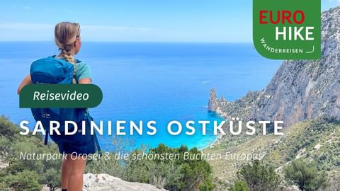 Wanderin mit Rucksack blickt auf das türkisfarbene Mittelmeer und felsige Küste Sardiniens. Felsklippen rahmen die Küstenansicht.