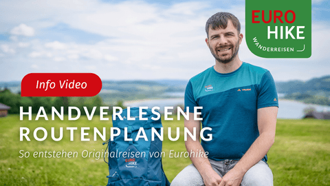 Mann in blauem Wandershirt sitzt im Freien mit Eurohike-Logo. Text lautet 'Info Video' und 'Handverlesene Routenplanung' vor Landschaft.