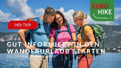 Drei Wanderer mit Rucksäcken schauen auf eine Karte am See mit Bergen im Hintergrund. Eurohike Logo und deutscher Text.