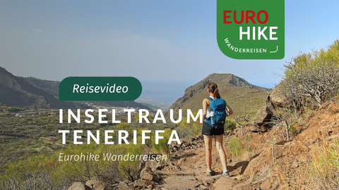 Wanderin mit blauem Rucksack auf felsigem Vulkanpfad auf Teneriffa mit Bergspitzen und Talblick unter klarem blauen Himmel.