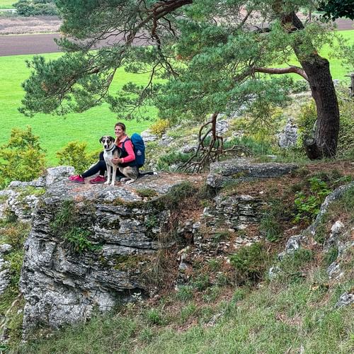 Hiker sits with dog on a rock and enjoys the view in the Altmühltal