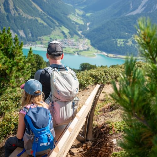 Familie sitzt auf Bank und genießt den Panoramablick auf den Reschensee