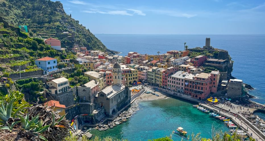 Vernazza village in Cinque Terre with colorful houses on a rocky peninsula, turquoise harbor, and historic tower overlooking the Mediterranean Sea.
