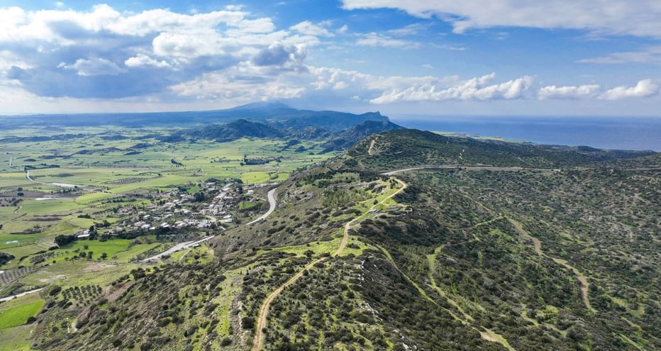 Luftaufnahme von sanften Hügeln und grünen Tälern auf Zypern bei Famagusta, mit gewundenen Feldwegen durch die Landschaft unter bewölktem Himmel.