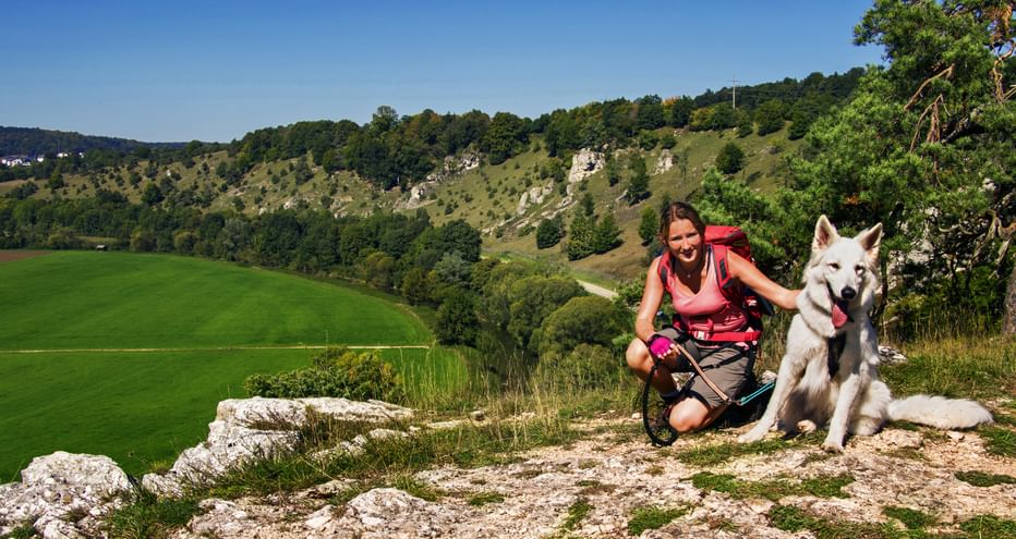 Knieende Wanderin mit sitzendem weißen Hund, im Hintergrund das Altmühltal