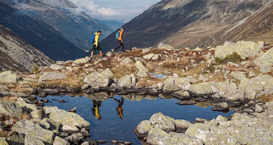 Reflection of two hikers in a mountain lake with panorama
