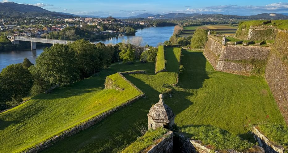 Luftaufnahme der Festung Valença mit Steinmauern und Wachturm, Blick auf Fluss mit Brücke und Stadt im Hintergrund unter blauem Himmel.