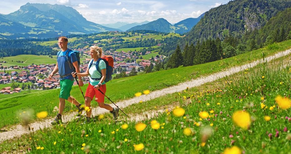 Hiking couple on panoramic path above Reit im Winkel with flower meadow in the foreground and mountains in the background