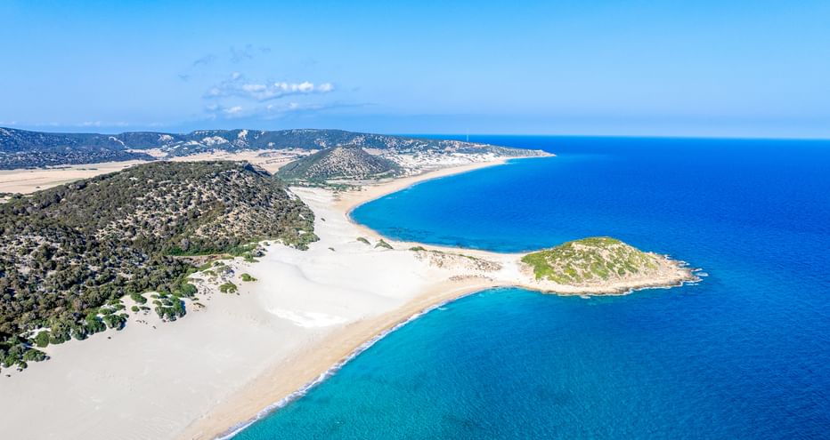 Luftaufnahme des Golden Beach auf der Halbinsel Karpaz, Zypern, mit weißen Sandstränden, türkisfarbenem Wasser und einer kleinen grünen Insel.