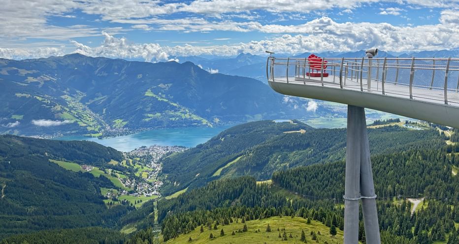Elevated viewing platform on Schmittenhöhe with visitors overlooking Zell am See lake, green mountains, and valleys in the Kitzbühel Alps.