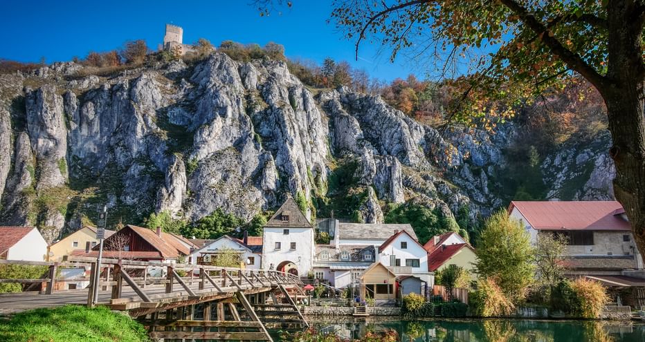 Dramatic white limestone cliffs rising above a village along the Main-Danube Canal in Altmühltal. Houses with red roofs nestle at the cliff base.