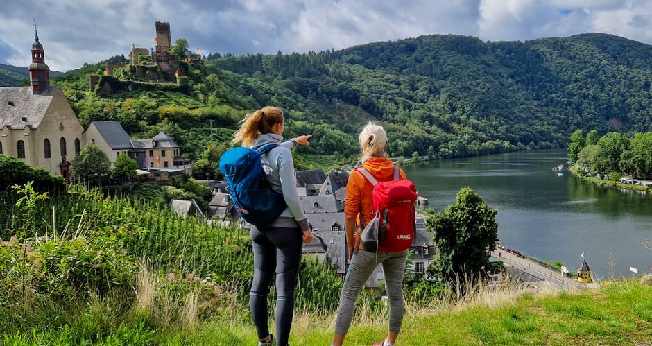 Blick auf Burg Metternich und Mosel mit Wanderinnen im Vordergrund