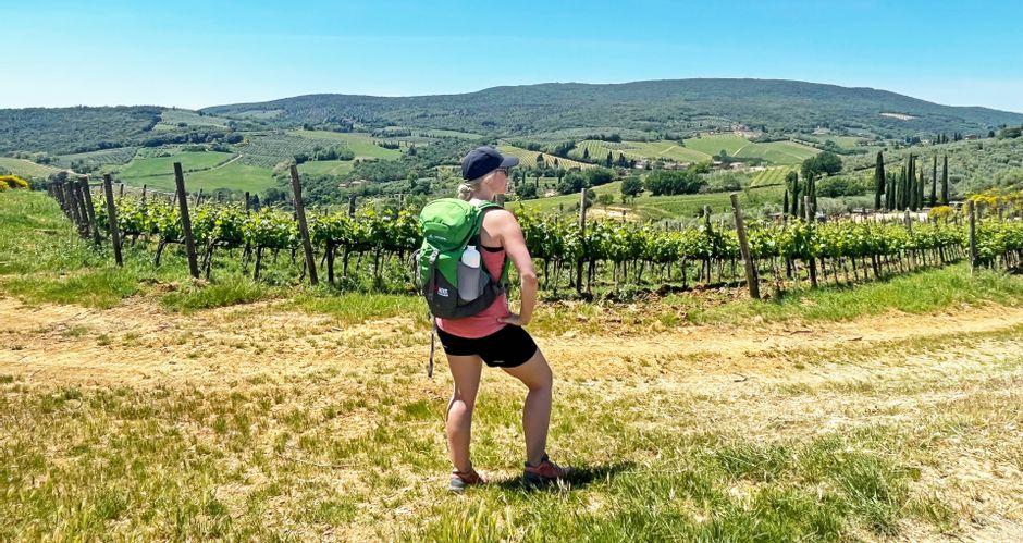 Wanderin vor Weinreben bei San Gimignano mit sanften Hügeln im Hintergrund