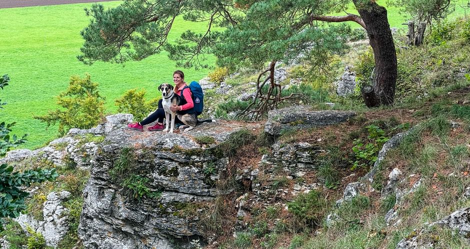 Wanderin sitz mit Hund auf einem Fels und genießt die Aussicht im Altmühltal