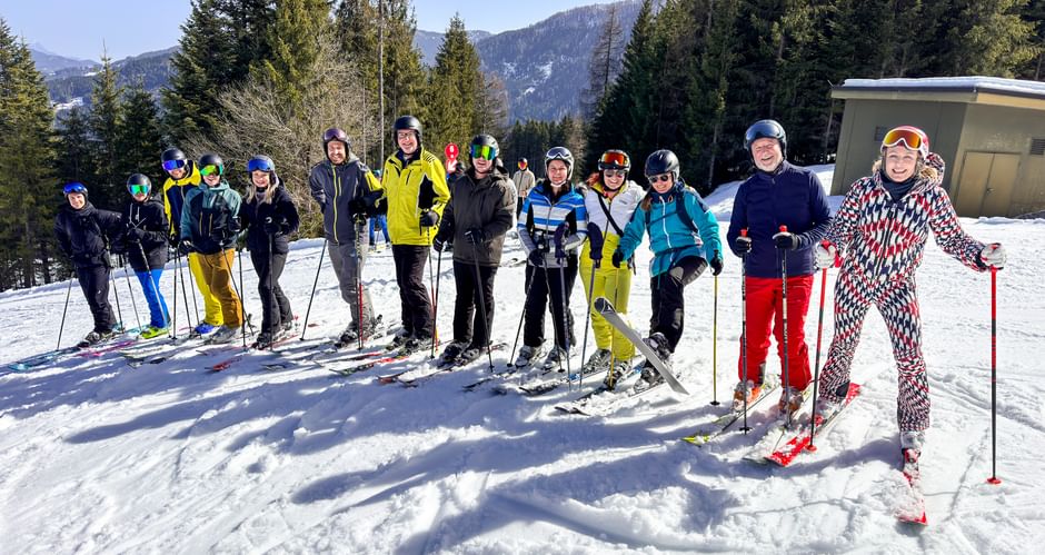 Gruppe von Skifahrern in bunter Winterkleidung posiert auf verschneiter Piste mit Wald und Bergen im Hintergrund beim Eurofun Touristik Wintersporttag 2026.