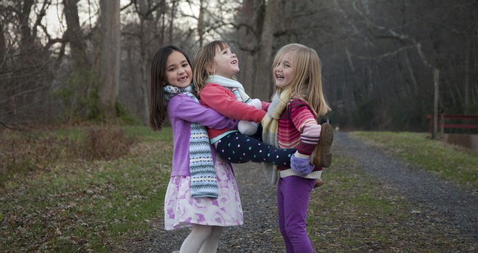 Drei kleine Mädls spielen gemeinsam im Wald und tragen die Kleinsten auf den Händen.