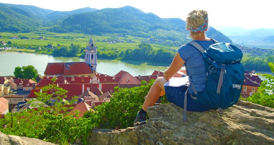 Wanderin bei einer Rast, sitzend auf einem Felsen oberhalb von Dürnstein und der Donau