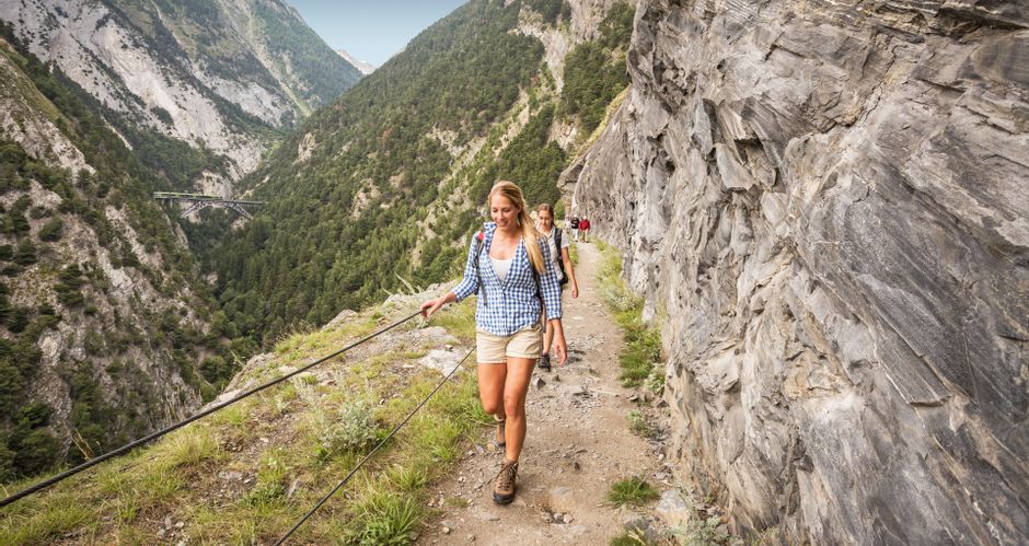 Wanderinnen auf gesichertem Wanderpfad entlang Felswänden auf der Lötschberger Südrampe