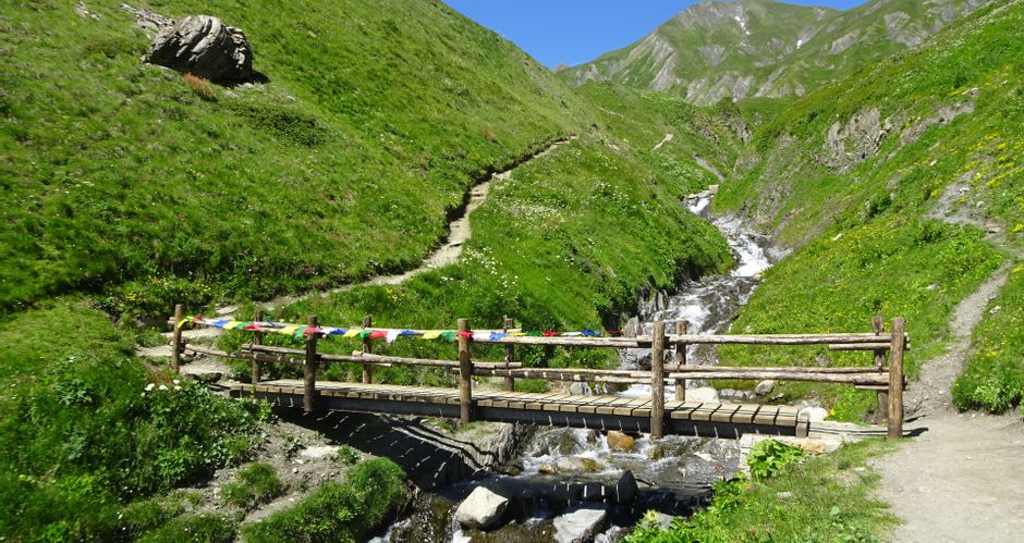 Narrow wooden bridge over a torrent with a view to the head of the valley on the hiking trail around Mont Blanc