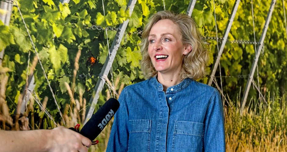 Blonde woman in a denim shirt laughs and speaks into a microphone