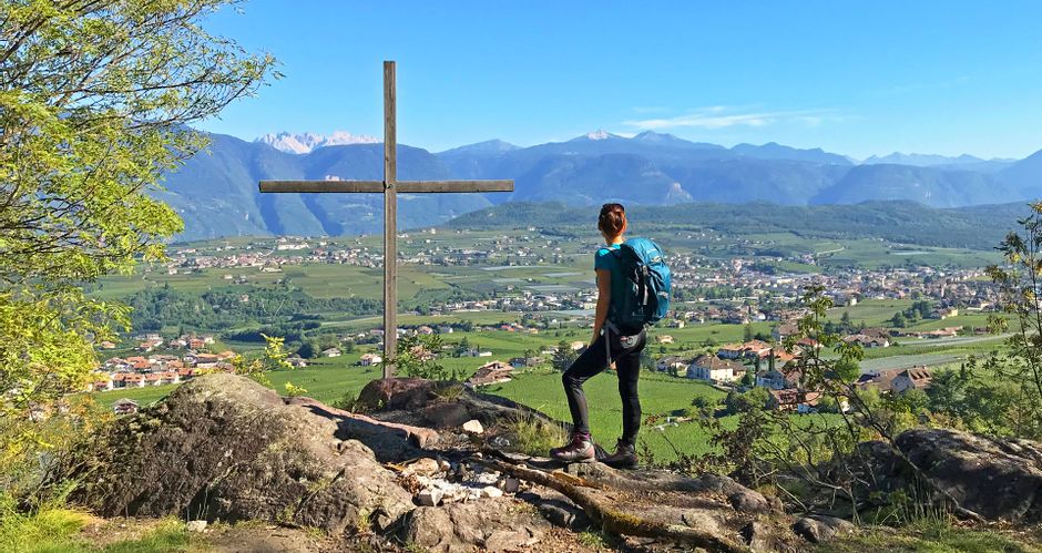 Wanderin bei einem Gipfelkreuz mit Blick auf das Etschtal