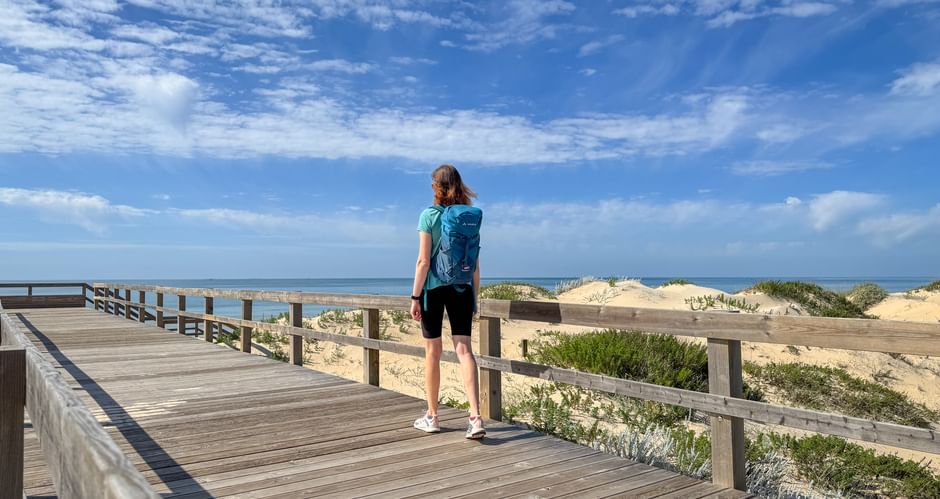 Wanderin wandert am Holzsteg entlang der Praia Verdelago am Meer